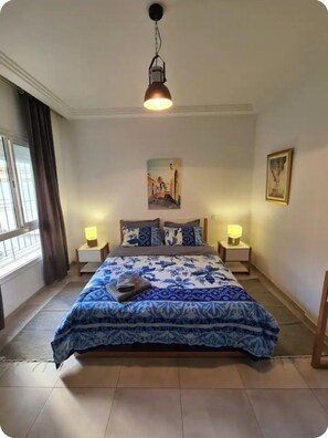 Une chambre à coucher avec un lit, deux lampes de chevet, un tableau au mur et une fenêtre avec des rideaux.