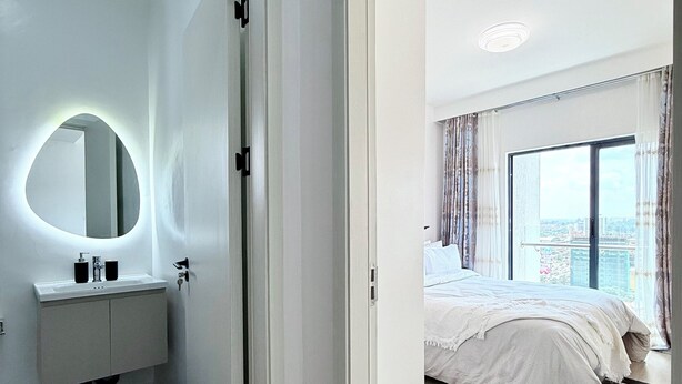 Un dormitorio moderno con una cama grande, un baño con un espejo redondo y vistas de la ciudad a través de un ventanal.
