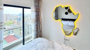 A hotel room with a large bed, a city view through the window, and a unique wall mirror. - Beautiful 1-bedroom apartment with fitness room in Nairobi (Nairobi)