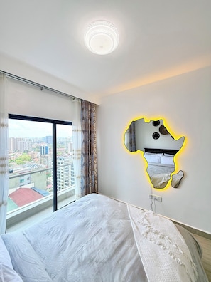 Une chambre d’hôtel avec un grand lit, une vue sur la ville par la fenêtre et un miroir mural original.