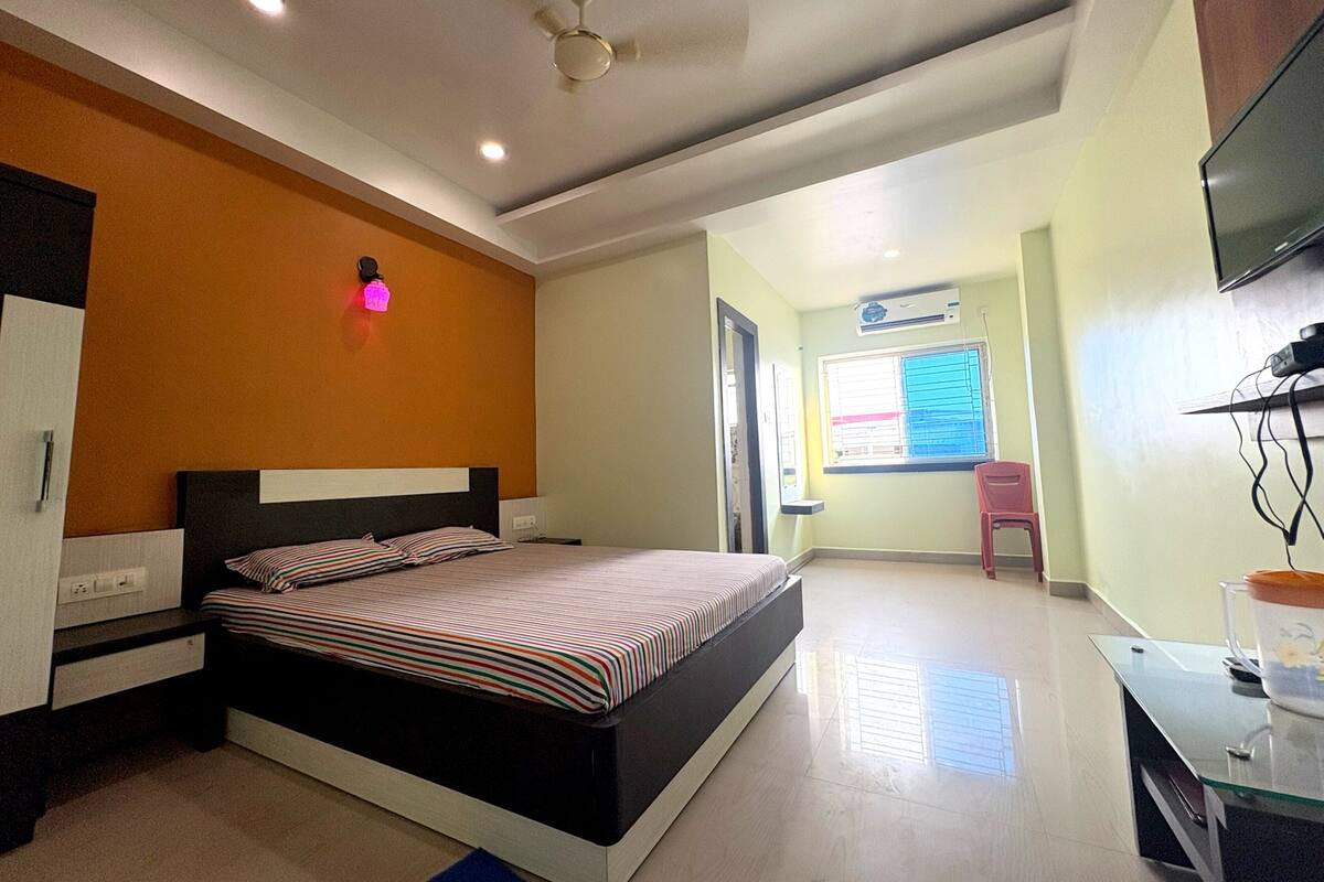 A modern bedroom with a bed, a desk, a chair, and a TV.