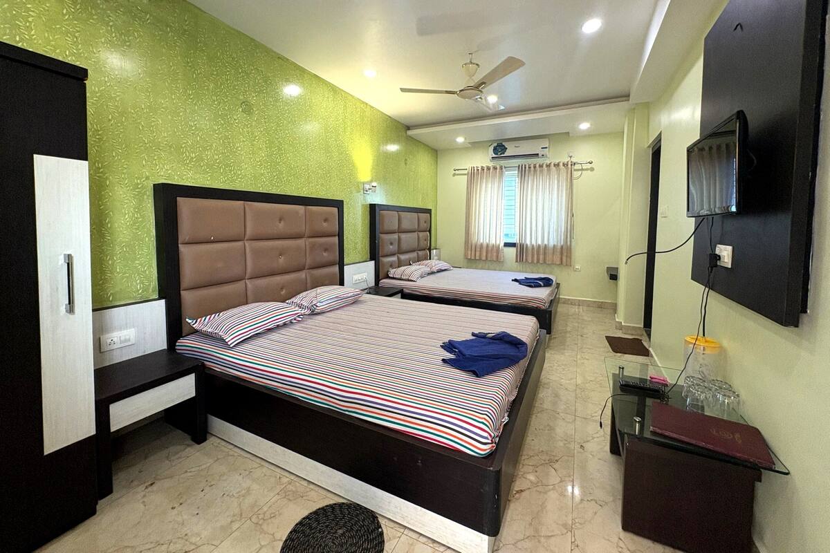 A hotel room with two beds, a ceiling fan, an air conditioning unit, a television, and a small table with glasses.