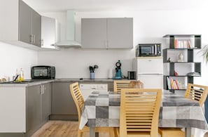 A compact kitchen with grey cabinets, a microwave, a toaster, and a dining table with a checkered tablecloth. - Downtown apartment 50m from the beach (Quiberon)
