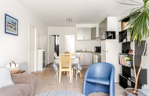 A modern living room with a sofa, a dining table with chairs, a blue armchair, a bookshelf, a potted plant, and a kitchen in the background. - Downtown apartment 50m from the beach (Quiberon)