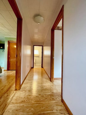 Ein Korridor mit Holzdielen, weißen Wänden und einer Decke mit eingelassener Beleuchtung.