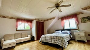 Une chambre à coucher comprenant un lit, un canapé, une table de chevet, un ventilateur de plafond et une fenêtre avec des rideaux.