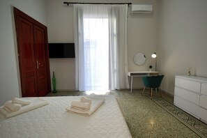 Ein Schlafzimmer mit Bett, Schreibtisch, Stuhl, Kleiderschrank, Flachbildfernseher und einem Fenster mit Vorhängen.