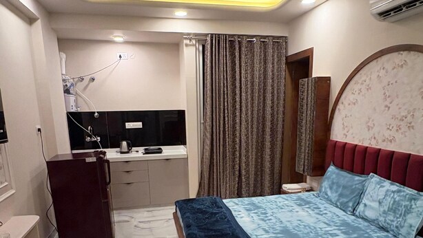A bedroom with a bed, a ceiling fan, an air conditioning unit, a small kitchenette, and a bathroom.
