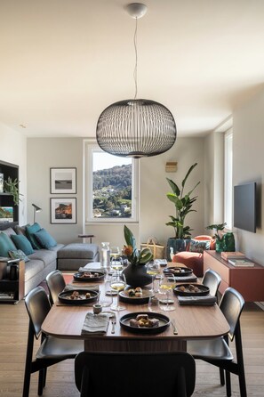 A dining area with a table set for a meal, a sofa, a TV, and a window with a view. - SAN PIETRO TERRACE BY THE SEA Seafront Luxury Terrace Apartment - Portovenere (Portovenere)