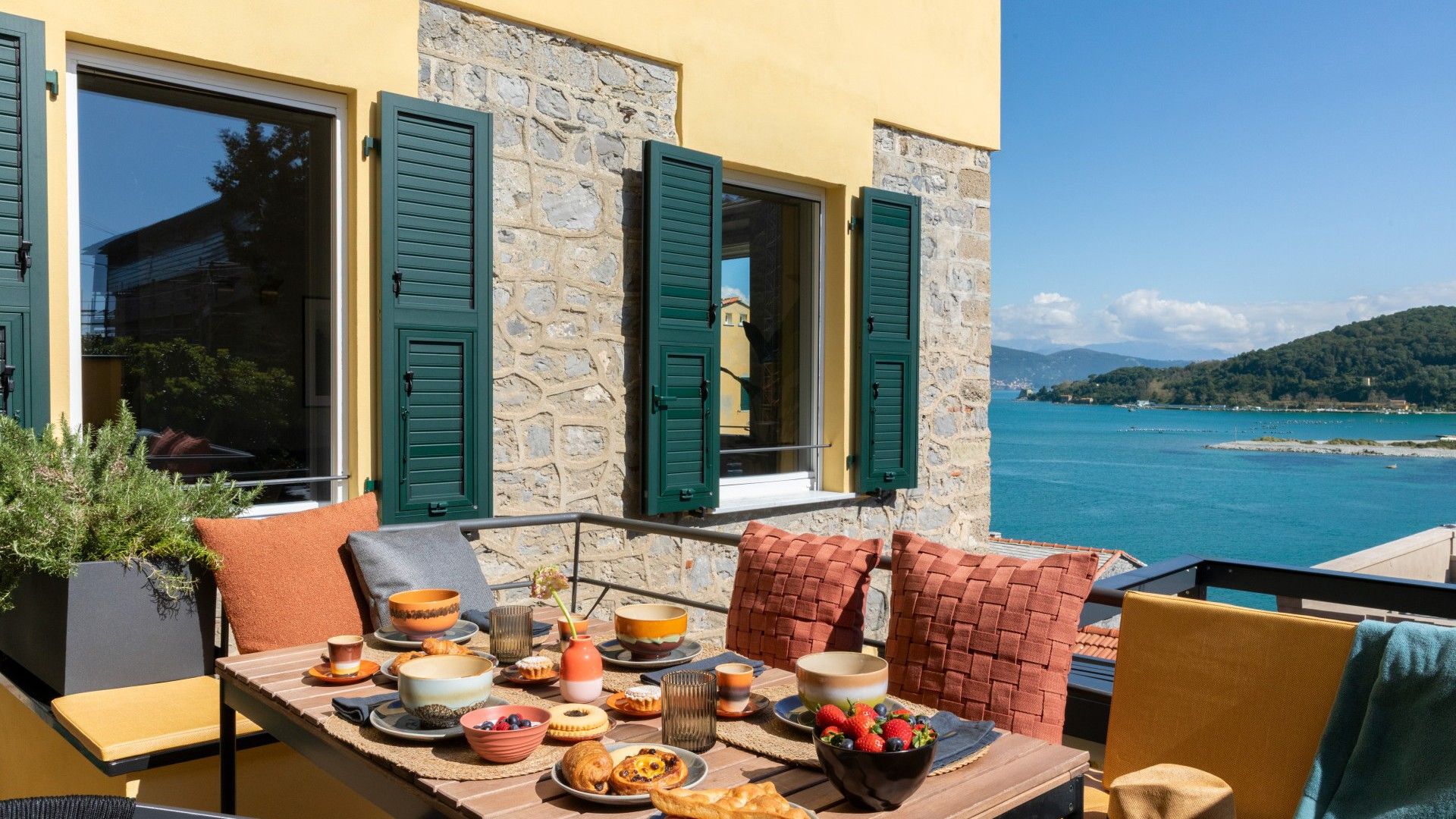 A terrace with a table set for breakfast overlooking a coastal view.