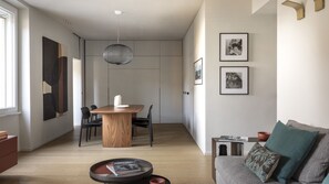 A modern living room with a wooden dining table, a sofa, and a coffee table. There are framed pictures on the wall and a pendant light above the table. - San Pietro Terrace by the Sea (Portovenere)
