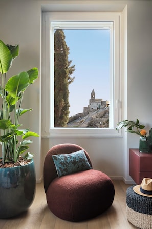 A room with a large window, a red chair, a potted plant, and a view of a building. - SAN PIETRO TERRACE BY THE SEA Seafront Luxury Terrace Apartment - Portovenere (Portovenere)