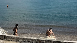 A coastal scene with a pebbled beach, calm sea, boats, and distant hills. - San Pietro Terrace by the Sea (Portovenere)