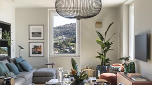 Un salon comprenant un canapé, une table basse, un téléviseur et une grande fenêtre donnant sur un paysage vallonné.