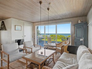 Una habitación con vista al mar, amoblada con un sofá, sillas y una mesa.