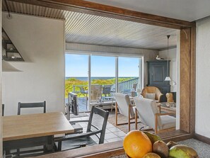 Una habitación con mesa de comedor, sillas, vista al océano y balcón con mobiliario exterior.