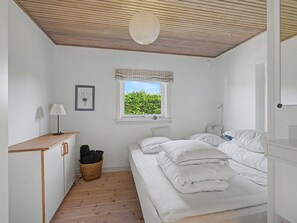 Un dormitorio con techo de madera, una ventana con vistas a zonas verdes, una mesita de noche con lámpara y una cama con ropa de cama blanca.