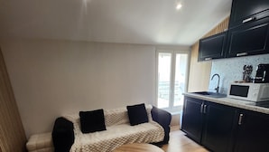 A compact living space with a sofa, a round coffee table, and a kitchenette area. - Superb small air-conditioned 2-bedroom apartment Ideally located (Avignon)