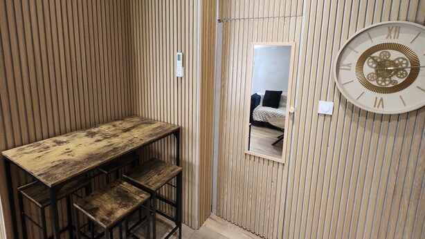 A room with a wooden slatted wall, a wooden table with chairs, a wall-mounted clock, and an air conditioning unit. - Superb small air-conditioned 2-bedroom apartment Ideally located (Avignon)