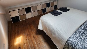 A bedroom with a sloped ceiling, wooden beams, a skylight, a bed with a patterned bedspread, and a built-in storage unit with multiple compartments. - Superb small air-conditioned 2-bedroom apartment Ideally located (Avignon)
