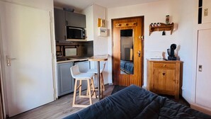 Een compacte kamer met een kitchenette, een klein eethoekje, een bed en een houten kast.
