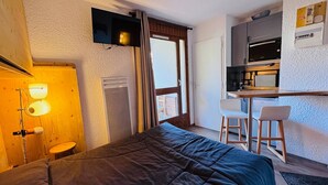 Een slaapkamer met een bed, een bureau, een stoel en een kitchenette.