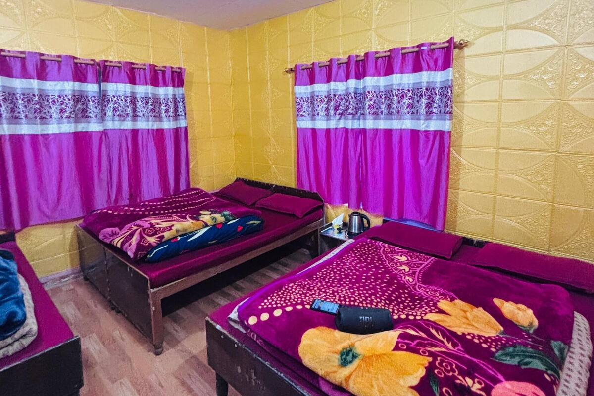 Quarto com três camas, cada uma com colcha e cortinas roxas combinando. As paredes são amarelas com um padrão geométrico.
