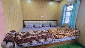 A bed with patterned bedding, a headboard, and a window with curtains. - Triple S Residency (Kedarnath)