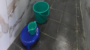 Un baño con inodoro, lavabo, calentador de agua y un cubo verde.