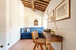 Ein Zimmer mit einem blauen Sofa, einem Holzstuhl, einem Schreibtisch mit einer Vase und gerahmten Bildern an der Wand.