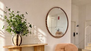Una habitación con una mesa consola de madera, un espejo redondo con marco a rayas, un sillón mullido y una planta en maceta.
