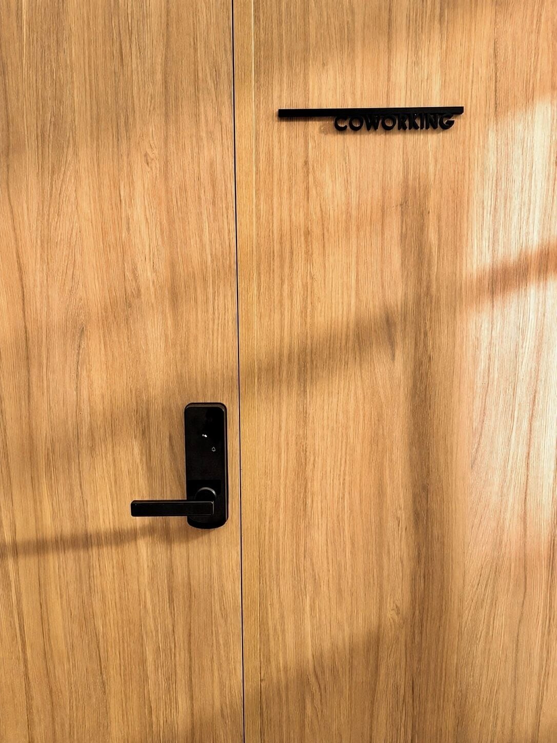 Une porte en bois avec une poignée noire et une pancarte indiquant « ESPACE DE COWORKING ».