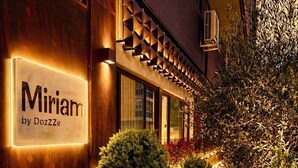 Un edificio con un letrero que dice 'Miriam by Dozzze' y dos plantas en macetas al frente.