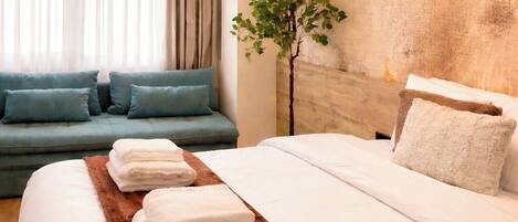 A hotel room with a bed, a sofa, a plant, and a window with curtains.