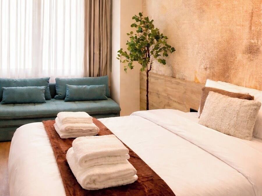 Ein Hotelzimmer mit Bett, Sofa, Pflanze und einem Fenster mit Vorhängen.