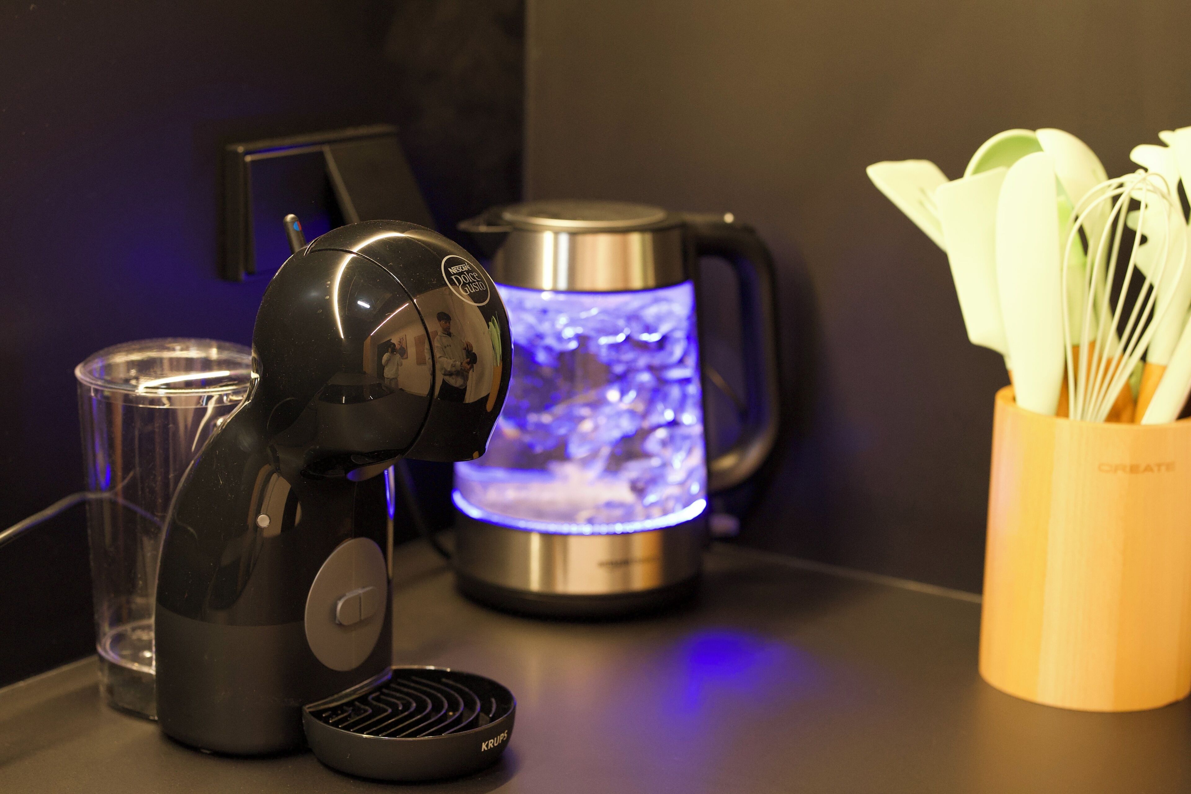 Una cafetera, un hervidor y un recipiente con utensilios sobre una encimera.