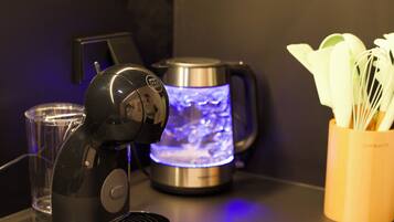 Una cafetera, un hervidor y un recipiente con utensilios sobre una encimera.