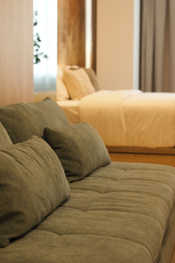Una habitació amb un sofà i un llit, amb roba de llit de tons clars.