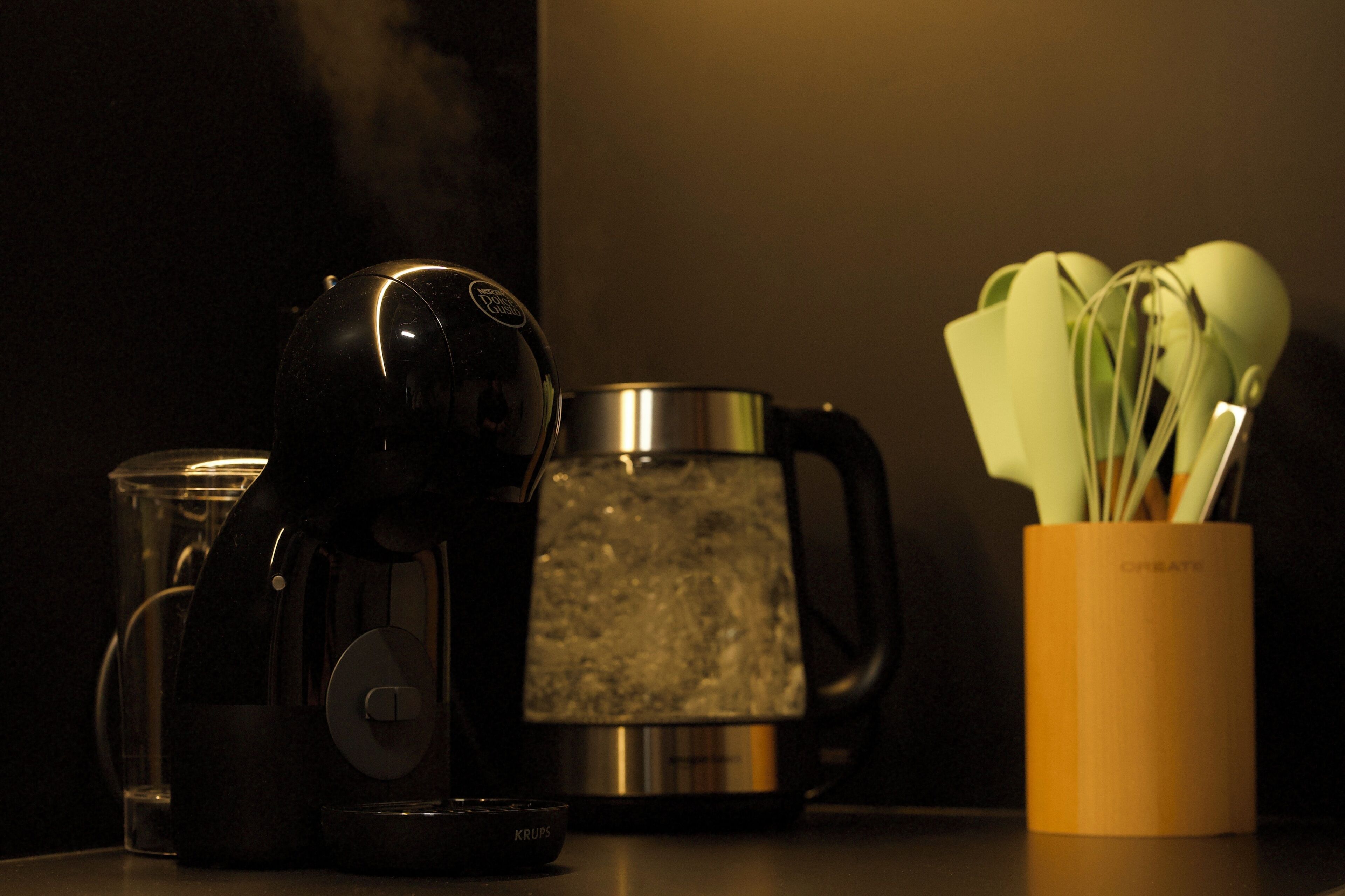 A coffee maker, a kettle, and a container with utensils on a countertop.