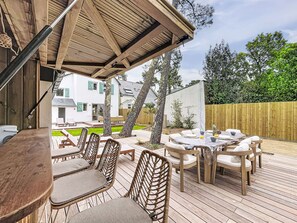 Eine Terrasse im Freien mit Holzmöbeln, einer überdachten Sitzgelegenheit und Blick auf ein Wohnhaus.