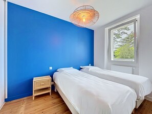 Ein Zimmer mit zwei Betten, einem Fenster, einem Wandheizkörper und einer Pendelleuchte.