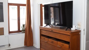 Ein Zimmer mit Fernseher auf einem Holzschrank, einem Fenster mit Vorhängen und einer Heizung.