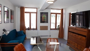 Ein modernes Wohnzimmer mit einer Couch, Sesseln, einem Glastisch, einem Fernseher und einem Schrank.