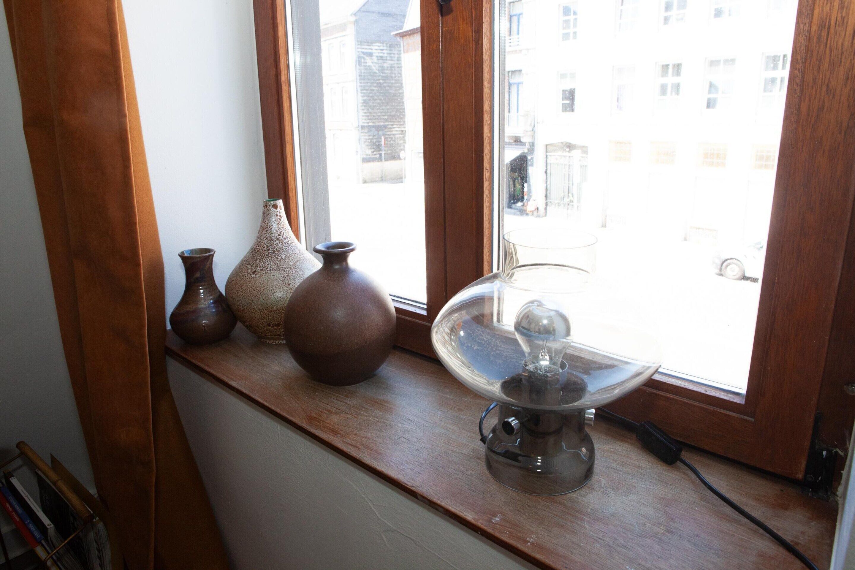 Ein Fensterbrett mit drei Vasen und einer Glaskuppenleuchte.