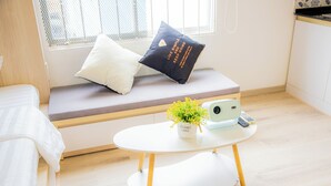 Quarto moderno com sofá-cama, uma pequena mesa redonda com uma planta, uma câmera e um travesseiro com uma frase motivacional.