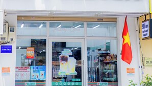 Uma loja 7-Eleven com uma placa grande, uma bandeira e fachada visível.