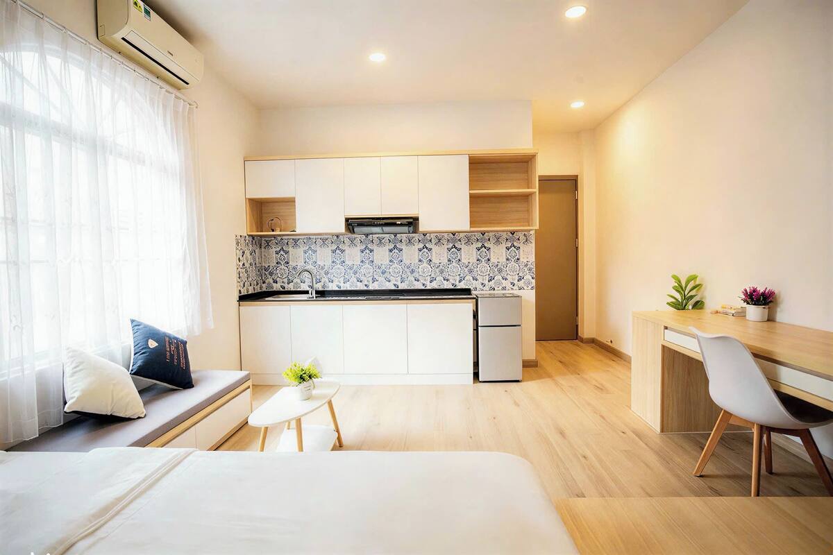 A compact hotel room with a kitchenette, a bed, a small table, and a desk area.