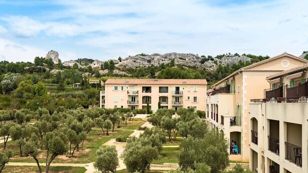 A building with multiple balconies, surrounded by olive trees and a mountainous backdrop. - Spacious Provence Retreat for 8 Guests (Paradou)
