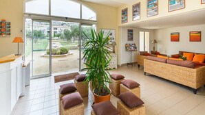 A spacious lobby with a large glass door leading to a courtyard, wicker furniture, and a reception desk. - Spacious Provence Retreat for 8 Guests (Paradou)