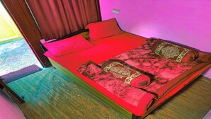 Una cama individual con una colcha y almohadas rojas, suelo de madera y pared rosa.